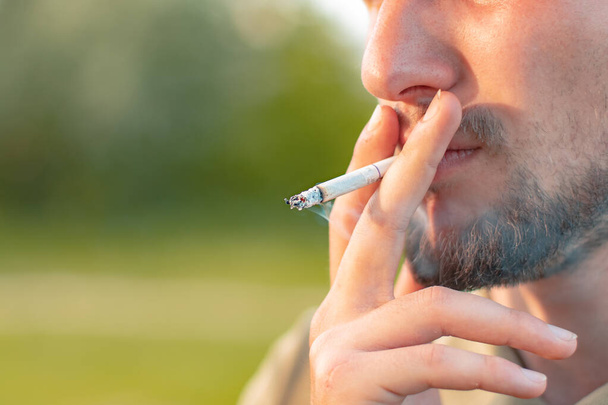 mau hábito fumar cigarro nos lábios do homem com fumaça ao ar livre perto retrato fotografia cartaz com espaço de cópia vazio para o seu texto aqui
 - Foto, Imagem