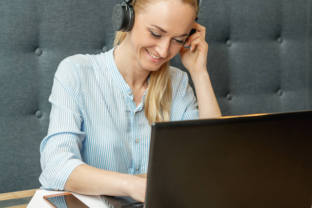 Ευτυχισμένη νεαρή γυναίκα φορώντας ακουστικά κοιτάζοντας στην οθόνη του φορητού υπολογιστή κατά τη διάρκεια της online κατάρτισης και βίντεο συνέδριο στο γραφείο στο σπίτι. - Φωτογραφία, εικόνα