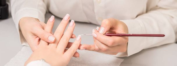 Dłoń młodej kobiety otrzymującej francuski manicure od kosmetyczki w salonie kosmetycznym. - Zdjęcie, obraz