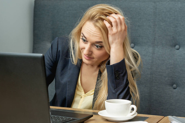 Zaniepokojona młoda kobieta wyglądająca na zaskoczoną podczas korzystania z laptopa w kawiarni. - Zdjęcie, obraz