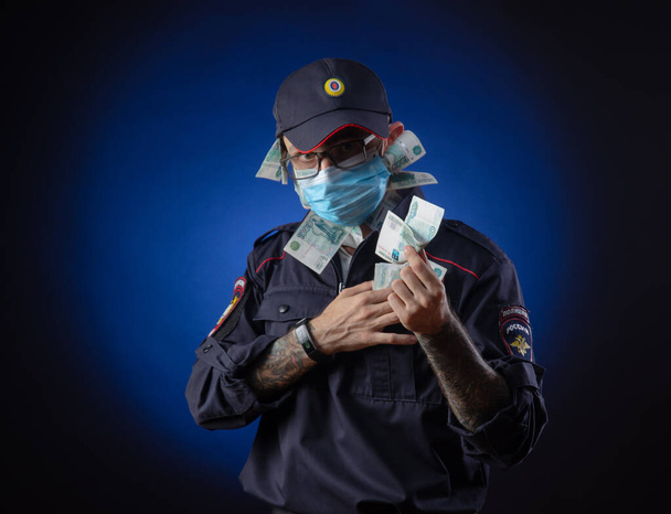 Ένας τύπος με στολή αστυνομικού Ρώσος αστυνομικός με ιατρική μάσκα με χρήματα στα χέρια του. Αγγλική μετάφραση του "Police" - Φωτογραφία, εικόνα