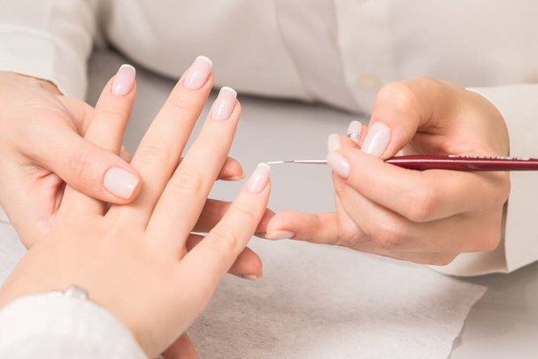 Hand einer jungen Frau erhält französische Maniküre von Kosmetikerin im Nagelstudio. - Foto, Bild