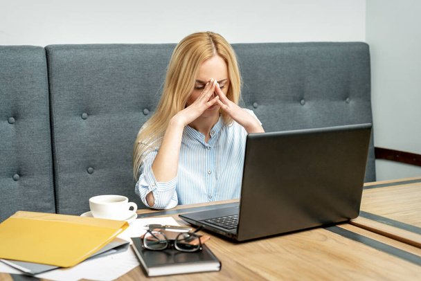 Ofiste dizüstü bilgisayarın önünde oturan yorgun genç iş kadını.. - Fotoğraf, Görsel