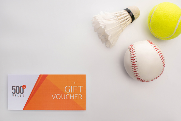 Top view of gift voucher near shuttlecock, tennis and cricket balls on white surface  - Foto, Bild