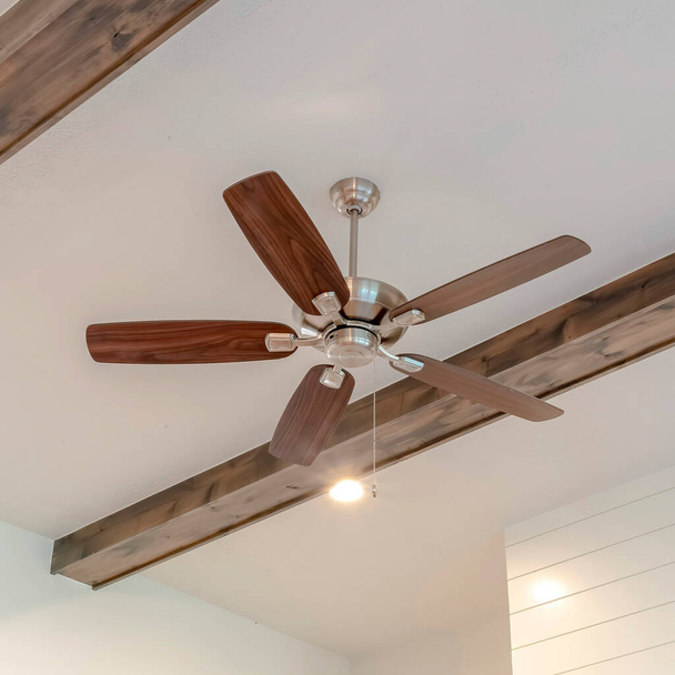 Ventilateur de plafond carré avec lumières entre poutres décoratives en bois à l'intérieur du salon de la maison - Photo, image