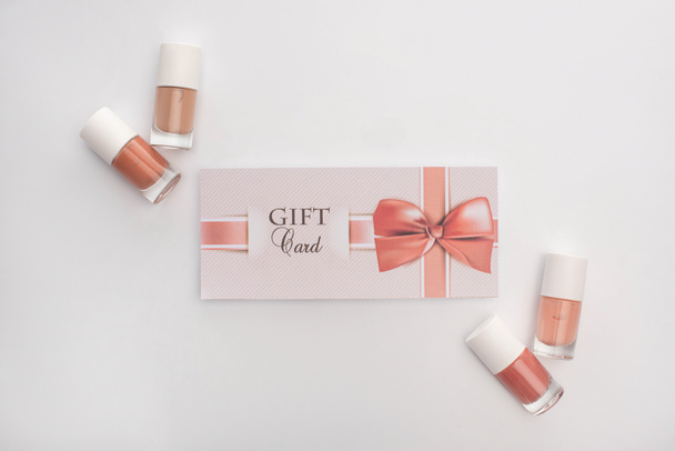 Top view of nail polishes and gift card with bow on white background - Fotoğraf, Görsel
