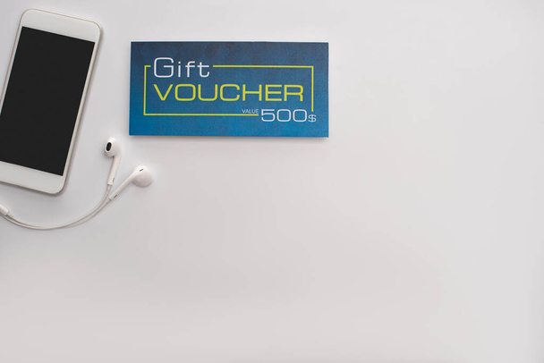 Top kilátás okostelefon közelében fülhallgató és ajándék utalvány fehér háttér - Fotó, kép