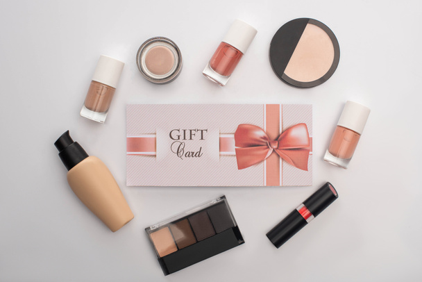 Top view of gift card near decorative cosmetics and nail polishes on white background - Photo, Image