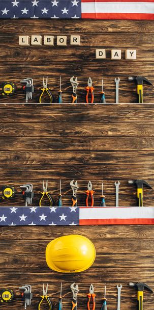 kolaż instrumentów, hełmów ochronnych i amerykańskich flag w pobliżu kostek z napisem z dnia roboczego na drewnianej powierzchni  - Zdjęcie, obraz