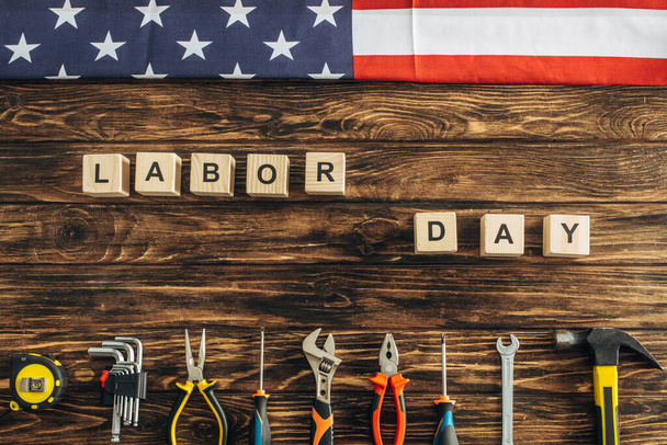 top view of metallic tools and american flag near cubes with labor day lettering on wooden surface  - Foto, imagen