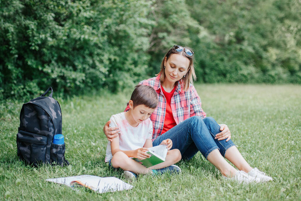 Jeune mère caucasienne lisant un livre avec son fils. Famille faisant des devoirs scolaires dans le parc en plein air. Maman aidant enfant enfant avec l'éducation apprendre à étudier. Développement précoce pour les enfants. - Photo, image