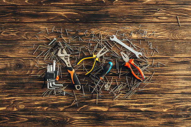 top view of instruments and metallic nails on wooden surface, labor day concept  - Foto, afbeelding