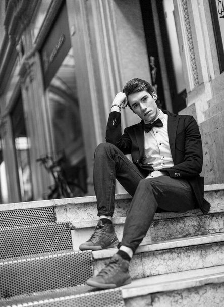 beautiful dark-haired boy poses in the center of reggio emilia with elegant shirt and pappillon jacket - Photo, Image