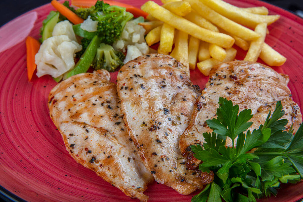 grilled chicken breast with green salad and french fries on a red plate. - Photo, Image