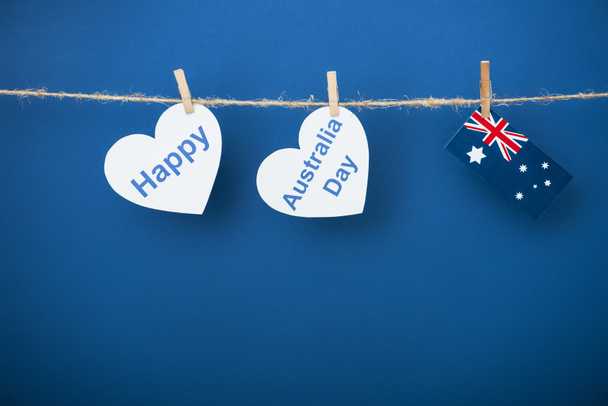 rope, clothespins and heart-shaped papers with happy near australia day lettering and flag on blue - Photo, Image