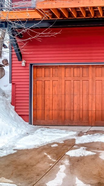 Κάθετο πλαίσιο Καφέ πόρτα γκαράζ και κόκκινο τοίχο του σπιτιού με χιονισμένη αυλή και δρόμο το χειμώνα - Φωτογραφία, εικόνα
