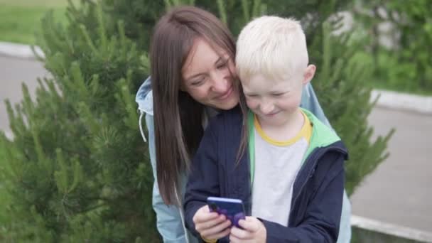 Een moeder en haar tienerzoon nemen een selfie op een mobiele telefoon op een wandeling in het park - Video