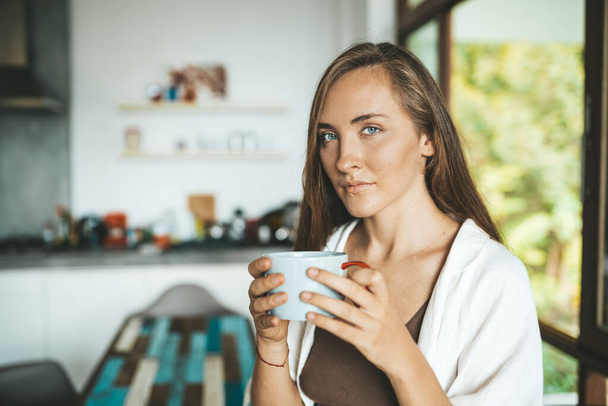 Smiling woman sitting in the kitchen and drinking coffee - Foto, immagini