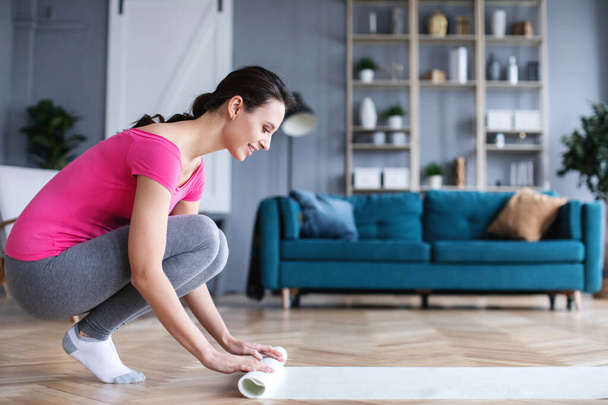 Woman rolls a yoga mat before doing indoor exercises. Home yoga. - Фото, зображення