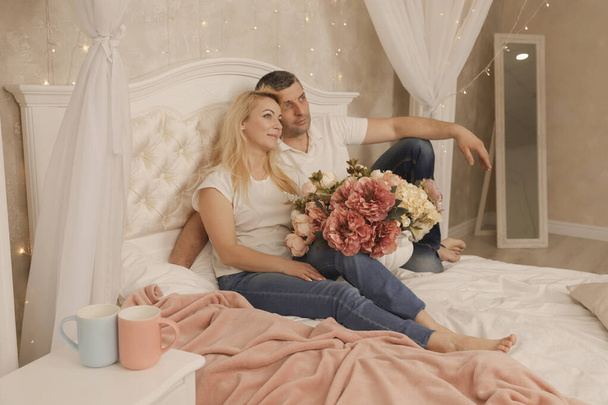 A férfi virágot és csókot ad a gyönyörű feleségének az ágyban. - Fotó, kép