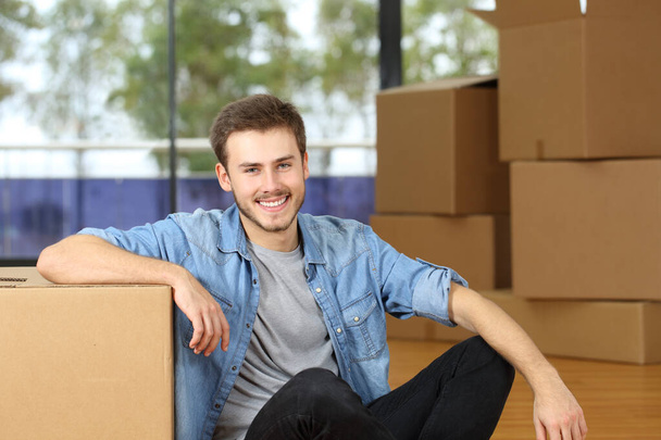 Happy man moving home looking at camera posing sitting on the floor with boxes - Foto, imagen