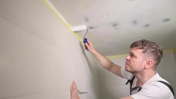 Työntekijä maalaus katto valkoisella maalilla. Maalari mies maalaa kylpyhuoneen kattoon telalla työkalu. Yleismies tyyppi käyttäen maalaustela. Korjaus asunnossa. Asunnon omistaja tekee remontin kotona. - Materiaali, video