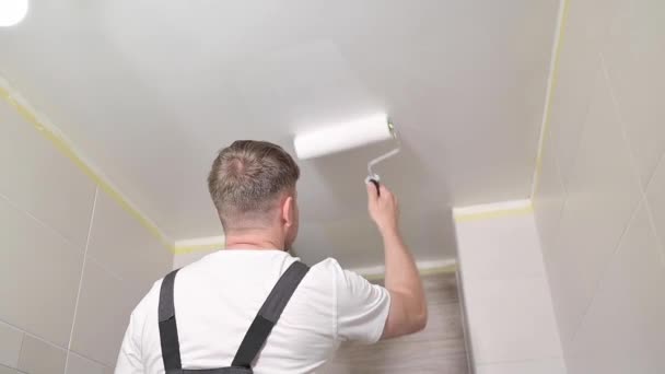 Werknemer schilderen plafond met witte verf. Schilder man schildert badkamer plafond met roller tool. Een klusjesman met verfroller. Reparatie in het appartement. Huiseigenaar renovatie reparatie thuis. - Video