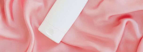 Blanco etiket cosmetische container fles als product mockup op roze zijde achtergrond - Foto, afbeelding