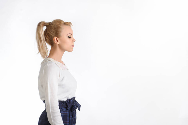 zijaanzicht van een 20-jarig blond meisje in witte blouse en blauwe rok op witte achtergrond denken over iets - Foto, afbeelding