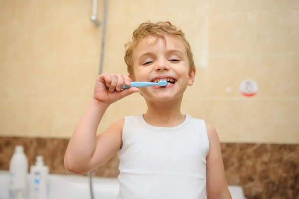 close-up foto van een blonde jongen schoonmaken van zijn tanden in een badkamer - Foto, afbeelding