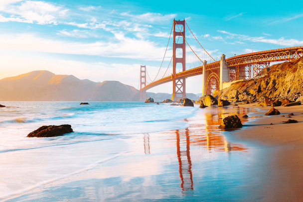 Classic panoramic view of famous Golden Gate Bridge seen from scenic Baker Beach in beautiful golden evening light on a sunny day with blue sky and clouds in summer, San Francisco, California, USA - Photo, Image