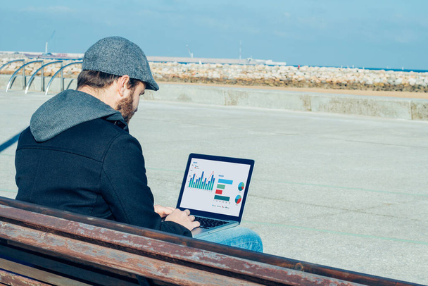 バック画面上のビジネスグラフィックとラップトップを使用して屋外に座っている男のビュー - 写真・画像