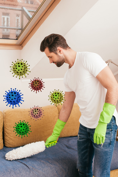 Boční pohled pohledného muže čistící gauč s prachem kartáč v obývacím pokoji, bakterie ilustrace - Fotografie, Obrázek