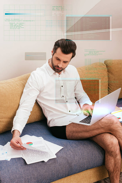 Handsome teleworker in panties and shirt working with documents and laptop on couch  - Photo, Image