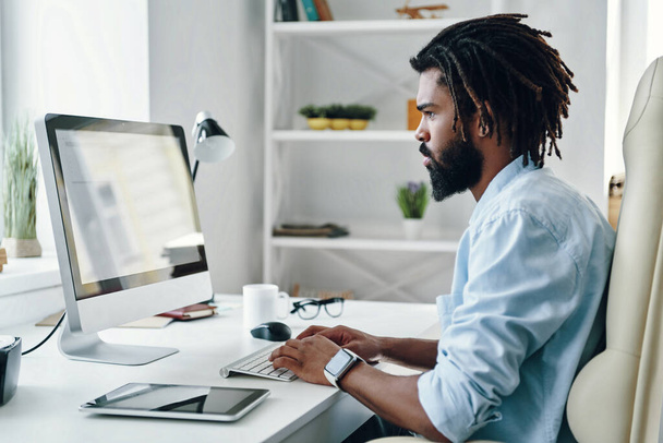 Thoughtful young African man using computer while working in the office - 写真・画像