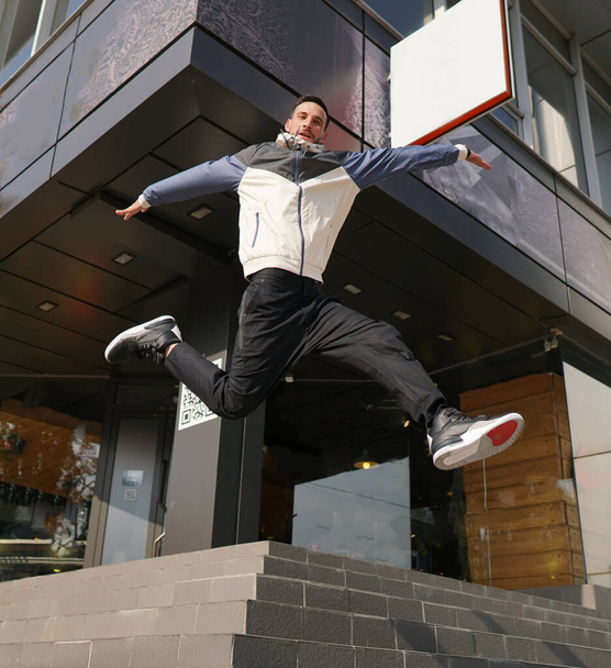 Giovane ragazzo attraente in posa davanti al negozio. Un uomo vestito di tre colori per allenarsi saltando dalle scale. Concetto di moda sportiva moderna. - Foto, immagini