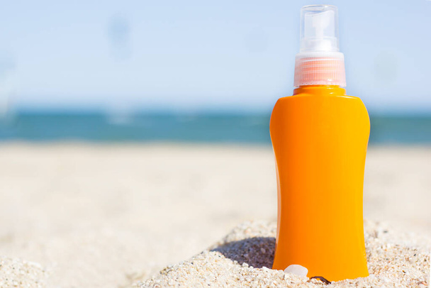 Orange Sunscreen Cream Bottle On The Beach. Summer time on the beach with sunblock. Sea and blue sky real background. Space for text. Skin protection during summer. Mock up. - Foto, Imagen