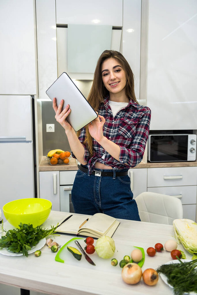 Giovane donna che utilizza un computer tablet per cucinare diverse verdure nella sua cucina per tutto ciò che riguarda una sana alimentazione - Foto, immagini