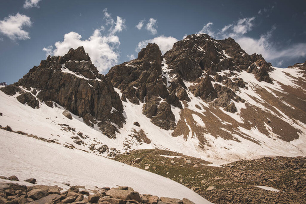 Tien Shan system in Kazakhstan near the city of Almaty. Rocky peaks covered with snow and glaciers in the middle of summer under clouds  - Foto, Imagem