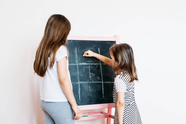 Two children, sisters, girls playing a game on a chalk Board, communication, development, home - Foto, Imagen