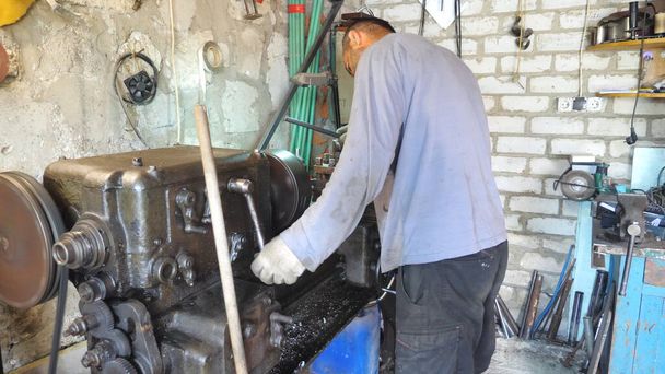 ガレージやワークショップで古いワークベンチで働く大人の男。金属加工のための旋盤を使用した機械。回転作業について表示します。スローモーションドリーショット. - 写真・画像