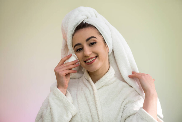 hermosa mujer joven en un albornoz y una toalla después de la ducha se está haciendo un cambio de imagen - aplicar polvo en la cara
. - Foto, imagen