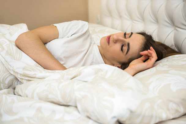 Genç bir kadın uyuyor ve tatlı rüyasını yatakta görüyor ve sabah işe gitmeden önce dinleniyor. Sağlık ve uyku konsepti - Fotoğraf, Görsel