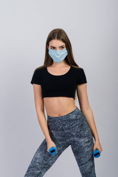 Giovane donna in maschera protettiva con manubri su sfondo bianco. Sport in quarantena - Foto, immagini