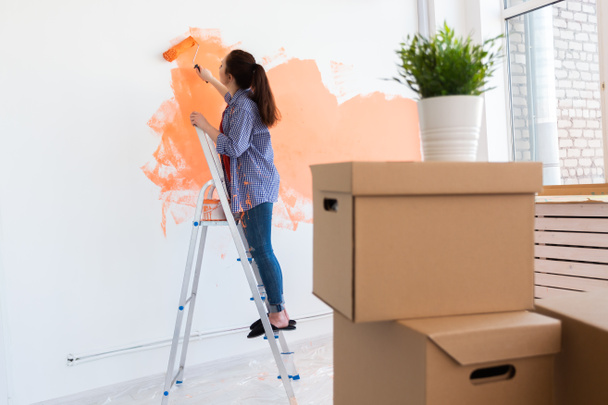 Vidám nő festi az új otthon falait. Felújítási, javítási és felújítási koncepció. - Fotó, kép