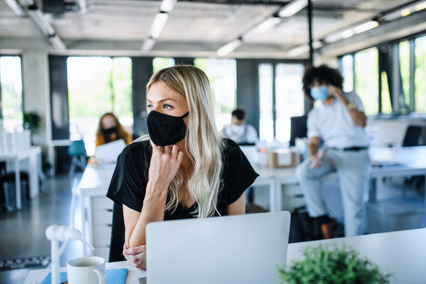 Young woman with face mask back at work in office after lockdown. - Φωτογραφία, εικόνα