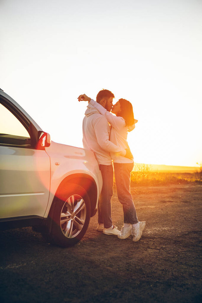 romanttinen hetki pari suudella auringonlaskussa lähellä valkoista suv auton kopiotilaa. - Valokuva, kuva