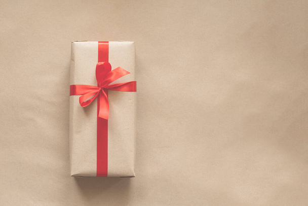 present wrapped in plain recycled paper with red ribbon on beige background - Foto, Bild
