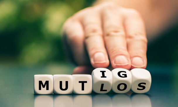Hand draait dobbelstenen en verandert het Duitse woord "mutlos" ("ontmoedigd") in "mutig" ("moed")"). - Foto, afbeelding
