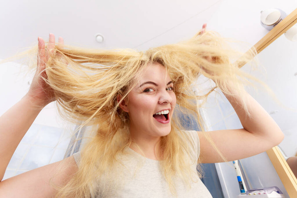 Happy woman having long blonde hair. Positive female after taking a shower feeling clean showing condition of her hairdo with joy - Fotografie, Obrázek